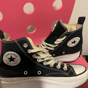 Svarta Converse All Star sneakers - Snygga svarta Converse All Star sneakers med hög sula och klassisk snörning. Skorna har den ikoniska logotypen på sidan och är perfekta för en avslappnad stil.