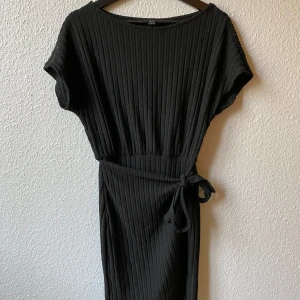 Svart ribbad klänning - Snygg svart ribbad klänning med knytband i midjan. Den har korta ärmar och en enkel, stilren design som passar perfekt för olika tillfällen.