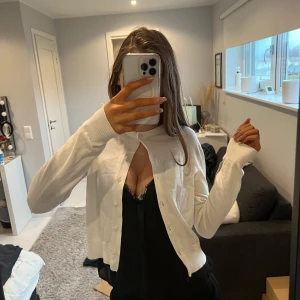 Vit kofta - Säljer en stilren vit kofta med knappar framtill. Perfekt för lager-på-lager och passar till många olika outfits. Koftan har långa ärmar och en klassisk design.