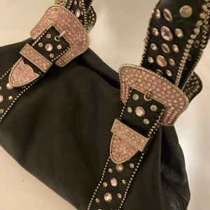 Snygg vintage väska med rhinestones - Snygg svart axelväska i skinn, fint skick med fina detaljer i lädret. Det är en äkta vintageväska och därav priset men går absolut att diskuteras. Väskan är ganska rymlig och man får plats med mycket.💕