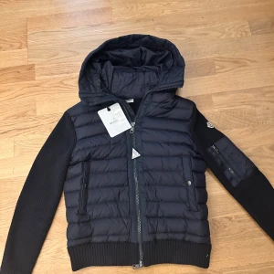 Svart jacka från Moncler - Snygg svart jacka från Moncler med quiltad design och dragkedja. Jackan har långa ärmar och en huva. Perfekt för kyligare dagar. 9/10 skick äkta från butik säljer på grund av att den nu är för liten.