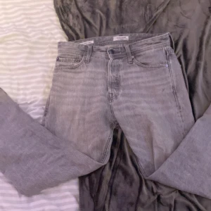 Grå jeans från Jack & Jones - Säljer ett par grå jeans från Jack & Jones, modell Relaxed/Chris. De har en avslappnad passform och är perfekta för en casual look. Den är i skick 7/10 då den används hyfsat mycket förra vintern. Den har inga fläckar eller stora skador men stygnen har gått upp lite längst ner på jeansen. 