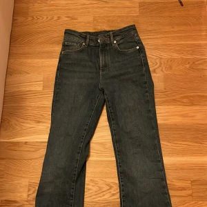 Blå jeansbyxor - Snygga blå jeansbyxor med bootcut-stil och hög midja. Perfekta för en avslappnad look. Klassisk design med fem fickor och knappgylf.
