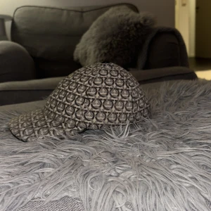 Mönstrad keps från Ferragamo - Snygg keps från Ferragamo med ett unikt mönster i beige och brunt. Kepsen har en justerbar rem baktill för perfekt passform. Perfekt för att ge din outfit en stilfull touch. Kvitto finns. Og 3300