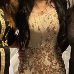 Beige långklänning med paljetter - Elegant beige långklänning dekorerad med glittriga paljetter i ett blommigt mönster. Klänningen har en figurnära passform och en vacker slits som ger en sofistikerad look. Strl S