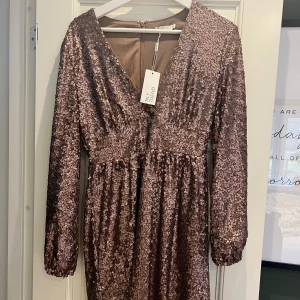 Glittrig klänning säljes. - Snygg glittrig klänning i en vacker brun nyans. Klänningen har långa ärmar och en dragkedja i ryggen. Perfekt för festliga tillfällen!