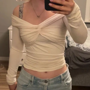 Beige offshoulder topp från Gina Tricot - Säljer en beige offshoulder topp från Gina Tricot. Toppen har långa ärmar och en knutdetalj framtill. 