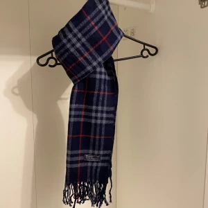Burberry - Säljer nu denna Snygga halsduk från Burberry i blått. Tillverkad i mjukt lammull med klassiskt fransad kant. Perfekt för att hålla dig varm och stilren under kyliga dagar. Hör av er vid funderingar☺️