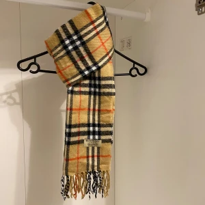 Burberry - Säljer nu denna Snygga och klassisk rutig halsduk från Burberry i beige. Tillverkad i mjukt lammull med fransar i ändarna. Perfekt för att hålla sig varm och stilren under kyliga dagar. Hör av er vid funderingar☺️