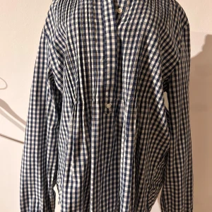 Blårutig  blus från Park Lane  med eleganta veck - Stilren, blårutig blus med långa ärmar och knappar framtill. Den har en klassisk krage och täta veck både på fram- och vbaksida vilka ger ett avslappnat fall. Perfekt för en avslappnad stil med en touch av finess.