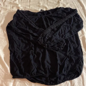 Svart topp från Ellos - Säljer en snygg svart topp från Ellos. Toppen har dekorativa detaljer längs ärmarna och en lös passform. Perfekt för en stilren look. Säljer då den inte kommer till användning. använd ett fåtal ggr.