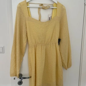 Ljusgul klänning från Nelly - Säljer en söt ljusgul klänning från Nelly med långa ärmar och knytband i ryggen. Klänningen har en fin struktur och en smickrande passform. Perfekt för vår och sommar!