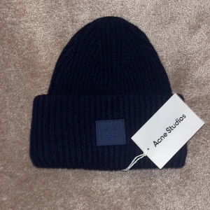 Mörkblå acne mössa - Snygg mörkblå ribbad mössa från Acne Studios. Perfekt för att hålla dig varm under kyliga dagar. Mössan är aldrig använd och är helt ny. Säljer för fel julklapp