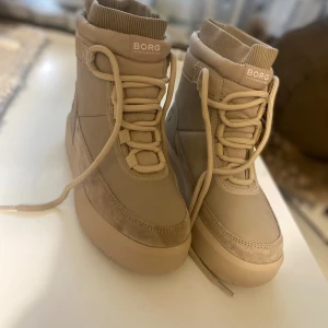 Beige boots från Borg - Snygga beige boots från Borg med snörning och ribbad kant upptill. Perfekta för kyligare dagar med sin robusta sula och stilrena design. De har en högre skaft och är gjorda i syntetmaterial. Ny skick! Aldrig använda. KÖPT FÖR 1500