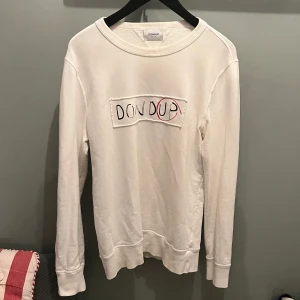 Vit långärmad tröja från Dondup - Säljer en stilren vit långärmad tröja från Dondup med ett broderat märke på bröstet. Perfekt för en avslappnad look.