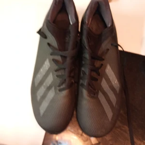 Svarta fotbollsskor från Adidas - Snygga svarta fotbollsskor från Adidas med klassiska ränder på sidan. Skorna har snörning för optimal passform och är perfekta för fotbollsplanen.