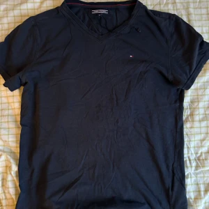 Svart t-shirt från Tommy Hilfiger - Snygg svart t-shirt från Tommy Hilfiger med v-ringning och liten logga på bröstet. Perfekt för en stilren look.