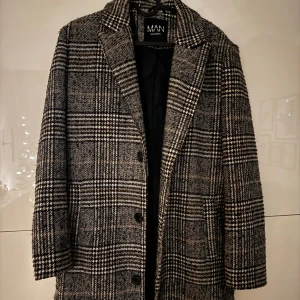 Rutig rock från BoohooMAN - Snygg rutig rock från BoohooMAN i svart och grått. Rocken har en klassisk krage och knappar framtill. Perfekt för höst och vinter med sitt stilrena mönster och långa ärmar.