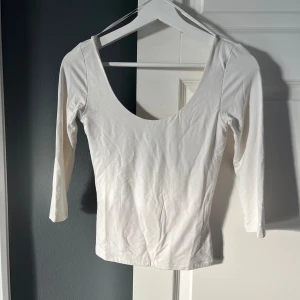 Vit topp från GinaTricot - Säljer en stilren vit topp från Gina Tricot med trekvartsärm, djup rund halsringning och korta ärmar.
