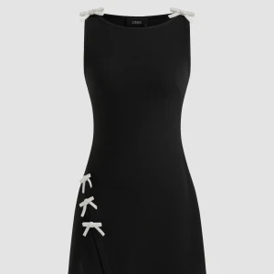 Svart klänning med glittriga detaljer  - Elegant svart klänning från Cider med glittriga rosetter på axlarna och sidan. Klänningen har en stilren design med en liten slits framtill. Perfekt för en festlig kväll!