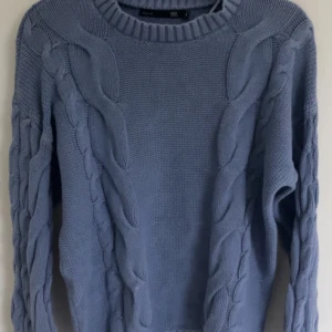 Blå stickad tröja med flätmönster - Säljer en snygg blå stickad tröja med flätmönster. Tröjan har långa ärmar och en rund halsringning. Perfekt för kyliga dagar! 