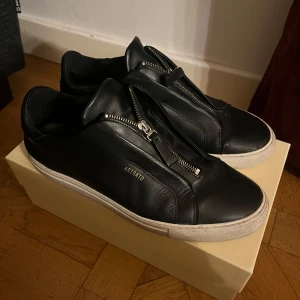 Axel Arigato skor - Snygga svarta sneakers från Axel Arigato med dragkedja framtill. Storlek 44, säljer då jag inte använder, de är i bra skick. Låda och skopåse finns.