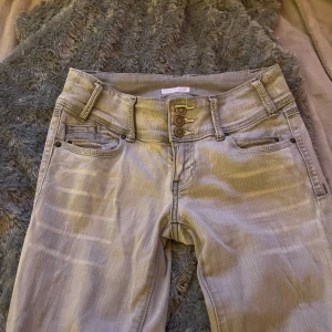Ljusgråa jeans med knappar - Snygga jeans med knappdetaljer. Stl 34, passar om man är omkring 165, lågmidjade.