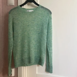 Grön stickad tröja från Zara - Säljer en mjuk och stilren grön stickad tröja från Zara. Tröjan har långa ärmar och ribbade kanter vid ärmslut och nederkant. Perfekt för en avslappnad look.