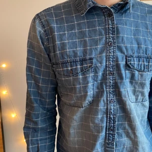 Blå rutig OVS skjorta  - Snygg blå rutig skjorta med långa ärmar och knappar framtill. Skjortan har två bröstfickor med knappstängning och en klassisk krage. Perfekt för en avslappnad stil.