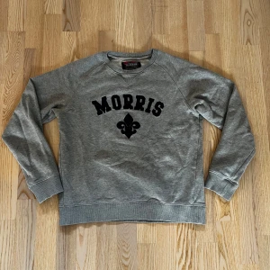 Grå sweatshirt från Morris - Snygg grå sweatshirt från Morris med klassiskt trycks på bröstet. Tillverkad i mjukt material och i fint skick, knappt använd. Perfekt för en avslappnad stil. Inga defekter och sitter bra. Storlek S men funkar för Xs också.