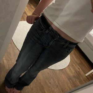 Blå jeans från H&M - Snygga blå jeans från H&M med en klassisk femficksdesign och knappgylf. Jeansen har en utsvängd passform och är perfekta för en avslappnad stil. De har en diskret tvätt för en modern look.