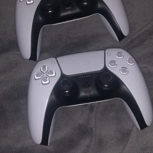 PlayStation 5 med två kontroller - Säljer en PlayStation 5 med två trådlösa DualSense-kontroller. Konsolen har en elegant vit och svart design med flera USB-portar för anslutning. Perfekt för gaming och underhållning.