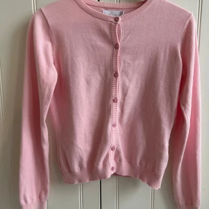 Rosa kofta från By Jeppson - Söt rosa kofta från By Jeppson med knappar framtill. Perfekt för lager-på-lager och att hålla sig varm under kyliga dagar. Den har långa ärmar och ribbade kanter för en bekväm passform. Använd någon enstaka gång. 