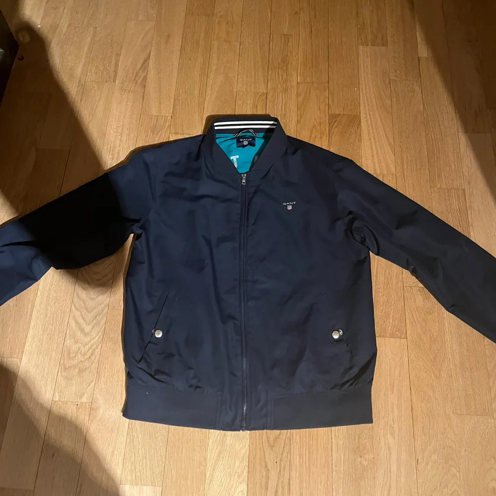 Snygg mörkblå bomberjacka från GANT med dragkedja och ribbade muddar. Jackan har två fickor med knappar och ett diskret GANT-märke på bröstet. Perfekt för en stilren look. skriv privat för bild på . Takit.
