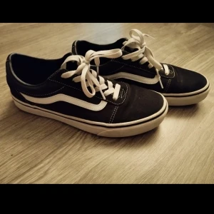 Svarta sneakers från Vans - Klassiska svarta sneakers från Vans med vit sula och snörning. Skorna har den ikoniska vita sidostripen och är perfekta för en avslappnad stil.