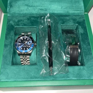 Lyxig klocka med blå och svart bezel - Snygg klocka med en tvåfärgad blå och svart bezel. Armbandet är i silverfärgat stål med en klassisk länkdesign. Klockan kommer i en elegant grön box med verktyg och extra länk. Klockan har inte används, köpte 2 olika och har valt att sälja denna. Även kvitto finns. 