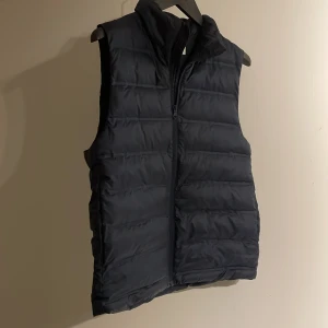 Svart dunväst från H&M - Säljer en stilren svart dunväst från H&M. Västen har en dragkedja framtill och är perfekt för kyligare dagar. Den quiltade designen ger ett modernt intryck och den är lätt att matcha med olika feta outfits🍸🥂