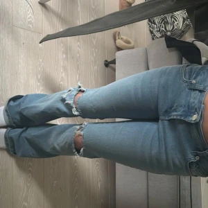 Blå jeans med slitningar - Snygga blå jeans med slitningar på knäna. De har en klassisk femficksdesign och en bekväm passform. Perfekta för en avslappnad stil.