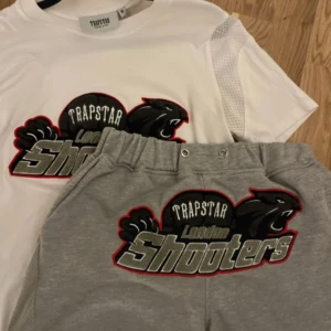 Grå shorts från Trapstar - Snygga grå shorts från Trapstar med ett coolt 'London Shooters' tryck i svart och rött. Perfekta för en avslappnad stil med en elastisk midja för extra komfort.