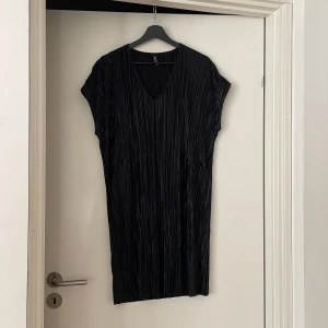 Svart plisserad klänning från Real - Snygg svart plisserad klänning från Real i storlek S. Klänningen har en v-ringad hals och korta ärmar, perfekt för en stilren look. Materialet ger en glansig finish som gör den extra speciell. Perfekt för att sticka ut med stil!