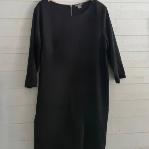 Svart klänning med guldig dragkedja oanvänd - Elegant svart klänning med trekvartsärm och en stilren dragkedja i ryggen. Perfekt för en chic och minimalistisk look. Helt oanvänd.