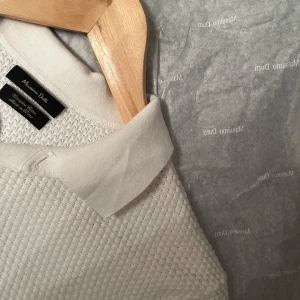 Vit pikétröja från Massimo Dutti - Säljer en stilren vit pikétröja från Massimo Dutti. Tröjan har en klassisk krage och knappar framtill. Materialet är texturerat vilket ger en unik känsla. Perfekt för en avslappnad men ändå elegant look.