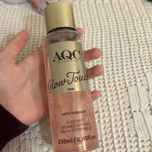 AQC Fragrances Glow Touch Pink Body Mist - Säljer en AQC Fragrances Glow Touch Pink body mist med shimmer. Flaskan är genomskinlig med en rosa vätska och har en guldig kork. Innehåller 250 ml och ger en glittrande effekt på huden.