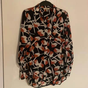 Mönstrad blus från Whyred - Säljer en snygg blus från Whyred med ett unikt mönster i svart, vitt och rött. Blusen har långa ärmar och knappar framtill. Perfekt för att ge din outfit en färgklick!