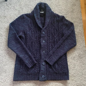 Mörkblå stickad cardigan - Säljer en snygg mörkblå stickad kofta med ett fint flätmönster. Koftan har långa ärmar och knappar framtill. Perfekt för kyliga dagar! Nypris runt 900kr mitt pris 449! Skick 9/10 ingen defekt eller annat. Priset är ej hugget i sten så kom med prisförslag, inga skambud! Storlek M men passar typ M-L nåt där i mellan.🤩😮‍💨