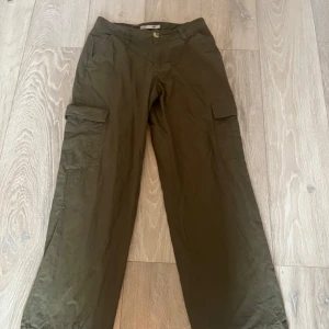 Olivgröna cargobyxor från 157 - Snygga olivgröna cargobyxor från 157 med praktiska fickor på sidorna. Perfekta för en avslappnad stil med en knapp och dragkedja i midjan. Byxorna har en loose passform och är tillverkade i ett bekvämt material.