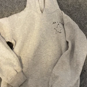 Grå hoodie från Gina Tricot - Säljer en grå hoodie från Gina Tricot med texten 'MA CHÉRIE' och en stjärna tryckt på framsidan. Tröjan har långa ärmar och en klassisk huva. Perfekt för en avslappnad stil. 🩶finns dock en liten fläck på ryggen som ej försvinner 