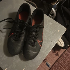 Svarta fotbollsskor från Nike - Säljer ett par svarta fotbollsskor från Nike med röda detaljer och snörning. Perfekta för fotbollsplanen med en stilren design och bra passform.