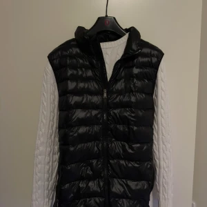 Svart dunväst från Polo Ralph Lauren - Snygg svart dunväst från Polo Ralph Lauren med dragkedja framtill. Perfekt för lager-på-lager under kyliga dagar. Klassisk design med quiltad stil som ger en stilren look.