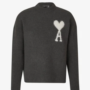 Mörkgrå tröja med hjärtmönster - Säljer en stilren mörkgrå tröja från Ami Paris med ett vitt hjärtmönster och bokstaven 'A' på bröstet. Tröjan har en klassisk passform med långa ärmar och ribbade kanter. Perfekt för kyliga dagar.